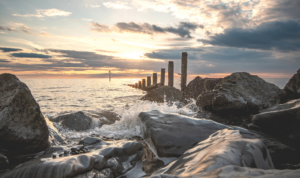 Photograph of gentle waves over rocks with an old wooden sea groyne and a pretty sunset.
