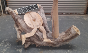 Sculpture made of driftwood pieces featuring small solar panel, a wooden clock and legs running with the caption - Time is running out.