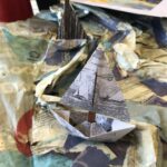 A paper boat with a picture of a boat on its sale sits in a paper sea.