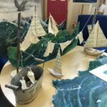Paper boats, a small washing line, a small in bath tub and cardboard waves arranged in a scene on a table.