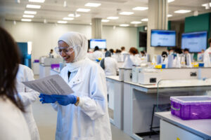 Young Muslim woman working in a science lab wearing a lab coat, gloves and goggles.