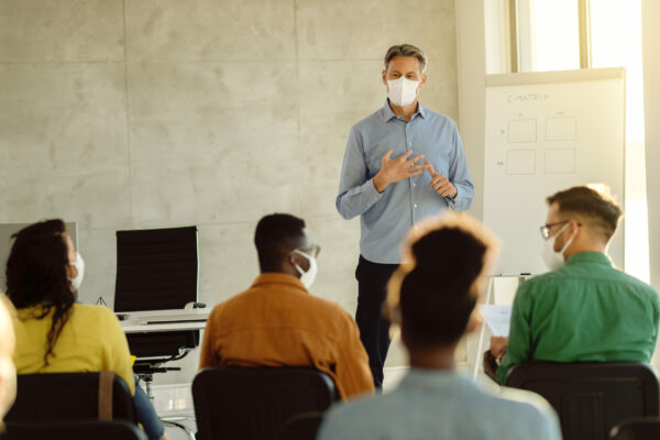 Teacher wearing protective face mask while holding a class to group of teachers during coronavirus epidemic.
