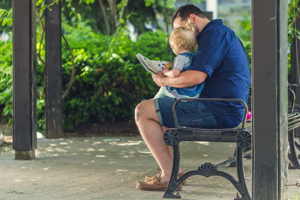 A father reads to his daughter on a bench.
