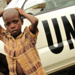 EBX2JR little boy standing in front of a car of the United Nations - Integrated Office of the United Nations in Burundi, Burundi, Bujumbura rural, Kabezi