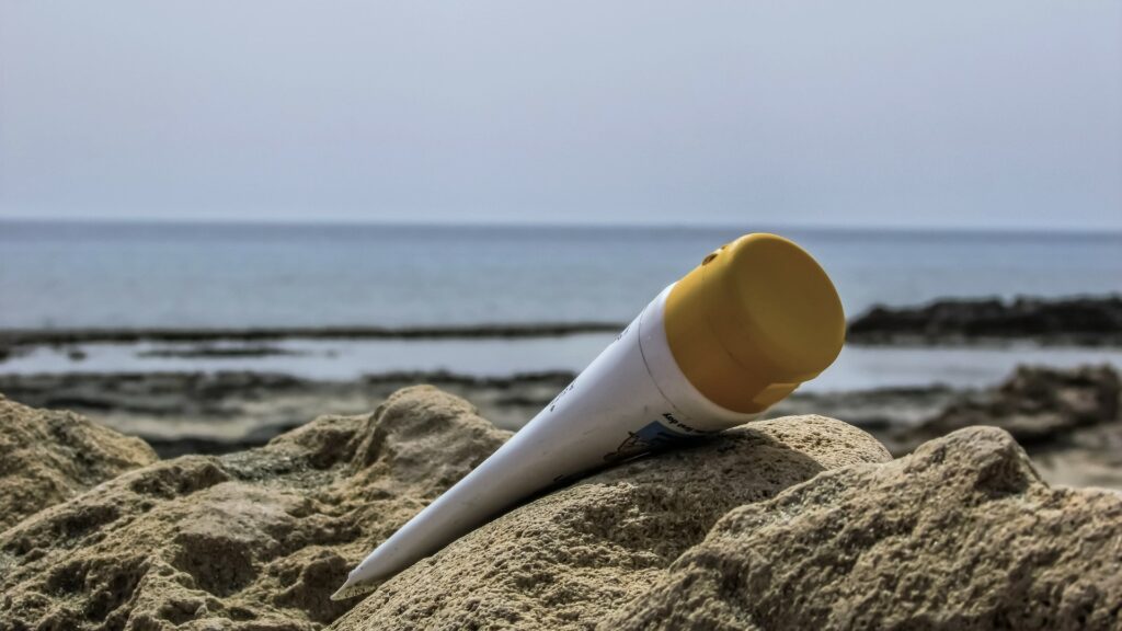 a bottle of sun cream lying on the sand on a beach