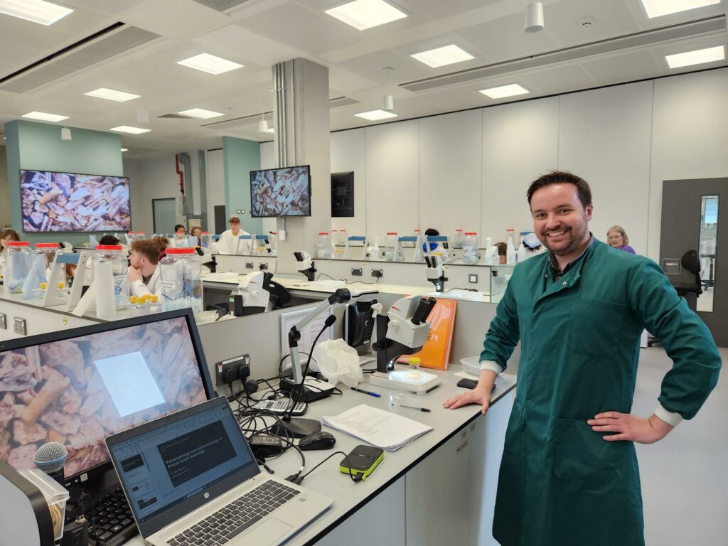 A smiling man in a green lab coat in a laboratory