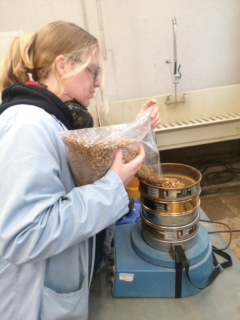 A woman in a labcoat pouring rocky samples into a machine for sorting