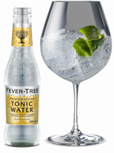 Small bottle of tonic next to gin glass containing ice and lime.