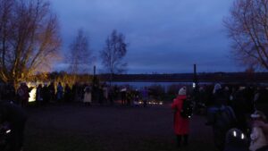 It is dusk and people are gathered by a ceremonial yule log in preparation for a theatrical performance