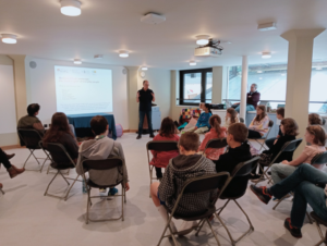 Professional male archaeologist talks through presentation to a group of seated children - members of Norwich Young Archaeologists' Club