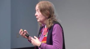 Eugenia Kalnay pictured from the slide, holding a laser pointer as she gives a talk