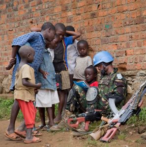 A peacekeeper of MONUSCO Force Intervention Brigade on foot patrol in the town of Pinga, North Kivu province, stops to interact with the local children. Pinga is located 148 km northwest of Goma, the provincial capital at the Rwandan border. Pinga was recently vacated by the local militia NDC (Nduma Defense of Congo) led by the rebel Ntabo Ntaberi Sheka. 4 December 2013. Photo: MONUSCO/Sylvain Liechti Un casque bleu de la Brigade d’intervention de la Force de la MONUSCO en patrouille à Pinga, en province du Nord Kivu, fait une pause pour communiquer avec un groupe d’enfants de la ville. Située à 148 km au Nord-Ouest de Goma, la capitale provinciale à la frontière avec le Rwanda, Pinga a été récemment désertée par la milice NDC (Nduma Défense du Congo) du chef rebelle Ntabo Ntaberi Sheka. 4 décembre 2013. Photo : MONUSCO/Sylvain Liechti