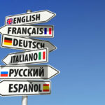 a signpost with signs for different languages in front of a bright blue sky
