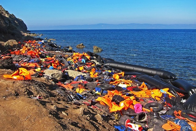 colour photograph of shore line with life jackets and boat wreckeage accumulated at tide mark