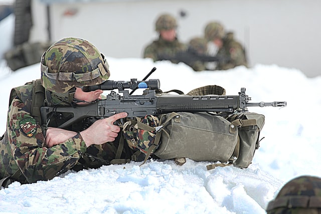 a soldier crouched in the snow aiming a gun
