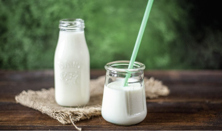 A glass jar of milk with a green straw in it. A glass bottle of milk stands in the background.