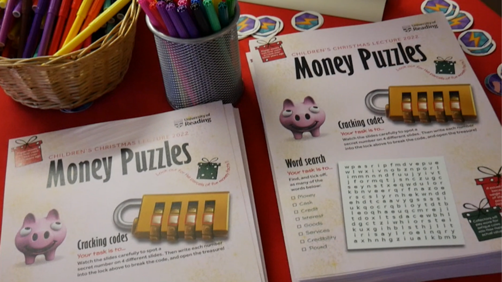 'Money puzzles' worksheets given out at the Christmas Children's lecture. The worksheets show a piggy bank, a padlock next to a 'cracking codes' puzzle and a word search.