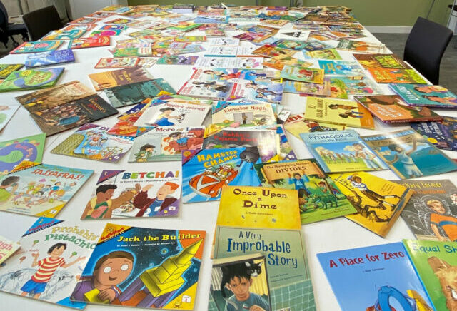 A selection of children's pictures with colourful covers spread out over a table. The books all have a maths theme.
