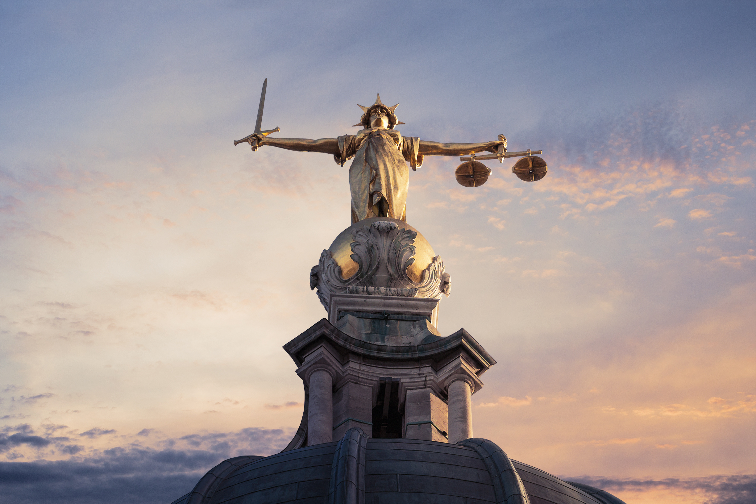 Gold Lady Justice Statue on the top of the Old Bailey in London, England, with a sunset sky in the background