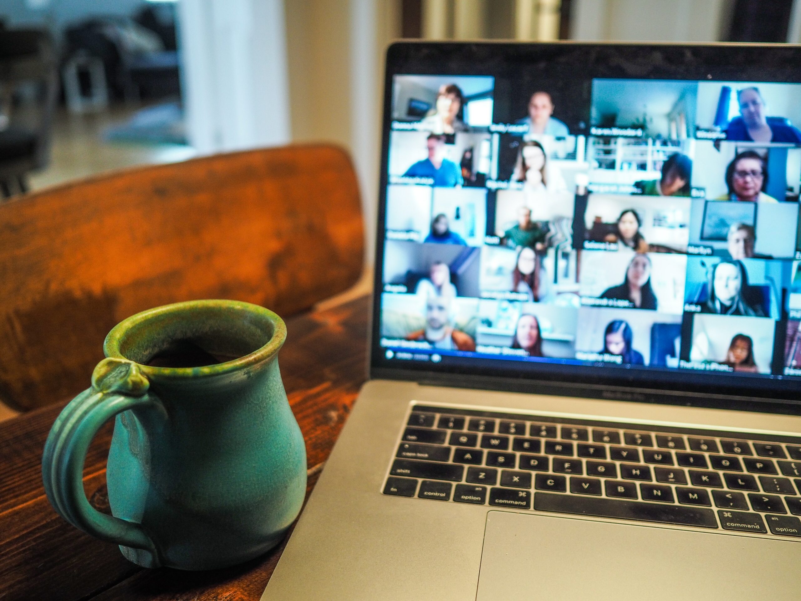 A laptop – showing a Zoom call with several people – next to a mug of coffee.