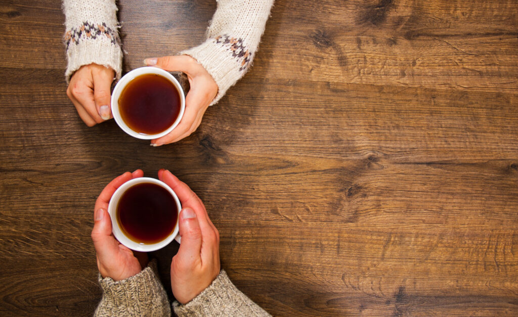 Cups of black tea in the hands of men and women. on a wooden background.