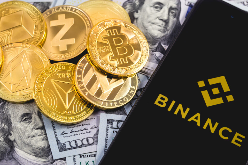 Phone with Binance logo, dollars, and gold coins representing cryptocurrency.