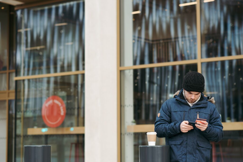 Man holds bank card and looks at phone outside of glass-fronted building