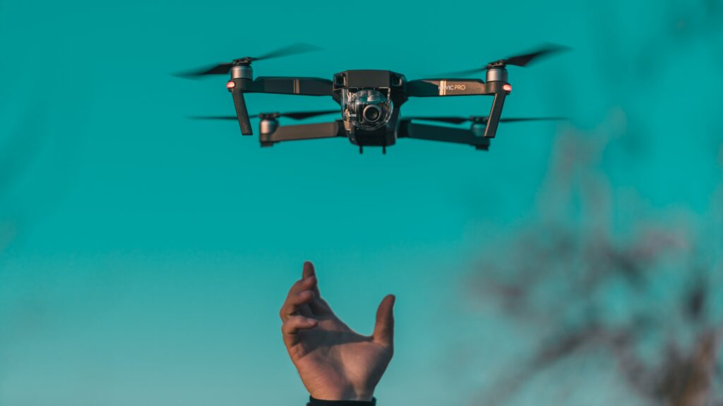 A drone flying against a blue sky with a hand in the foreground