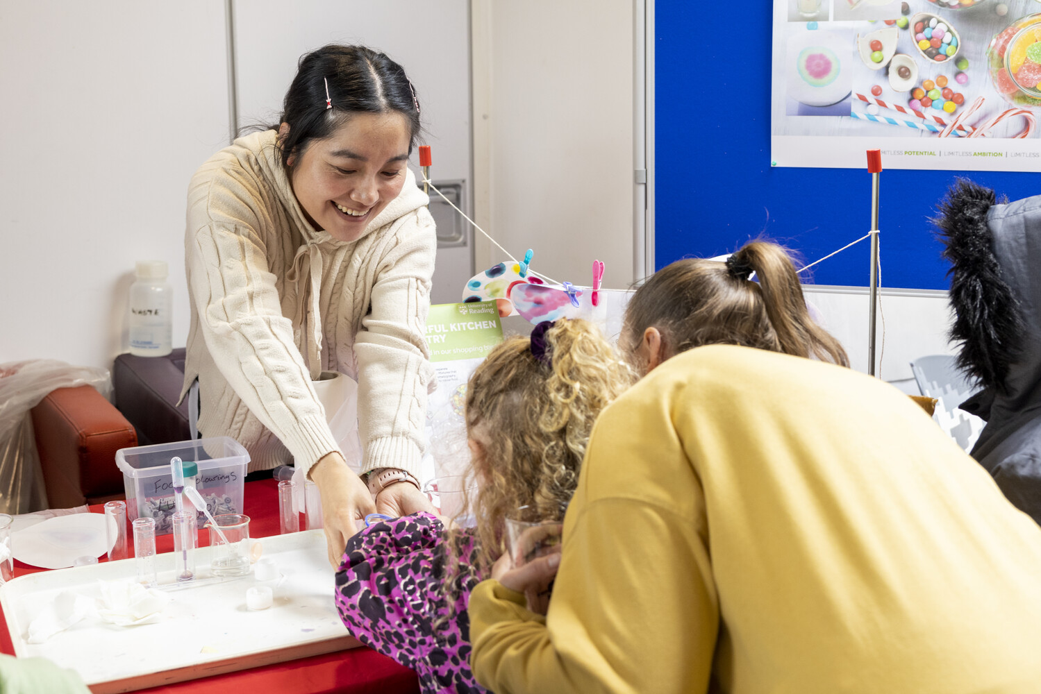 a researcher at the 2023 Community Festival engages with a child and their parents with pipettes and scientific equipment