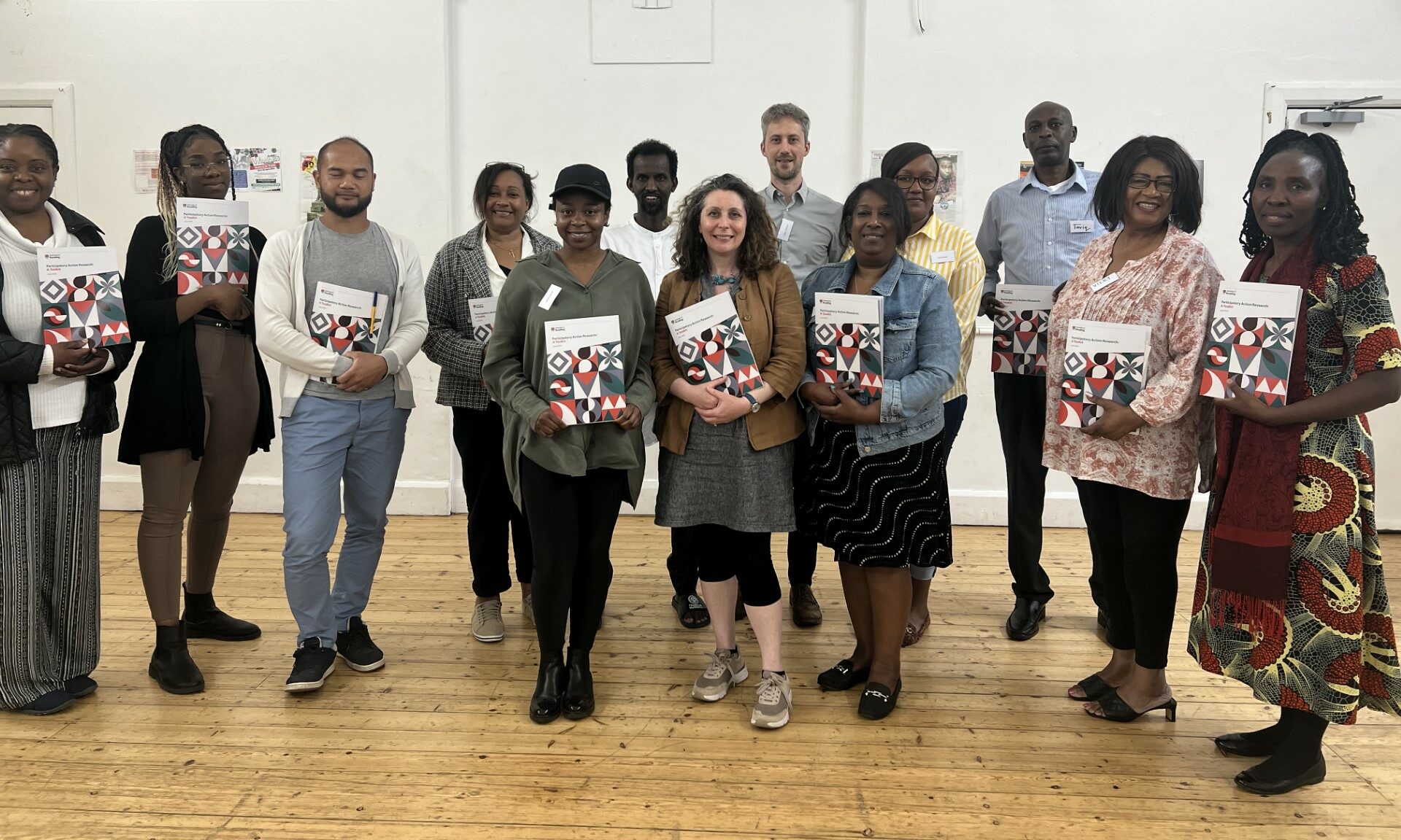 Community researchers and trainers pose for a group photo. They are standing, smiling at the camera and holding copies of Participatory Action Research: A Toolkit