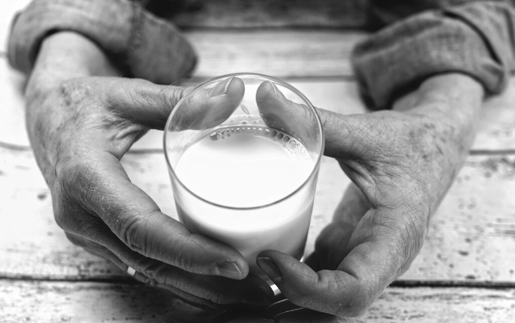 Hands of older person holding a glass of milk