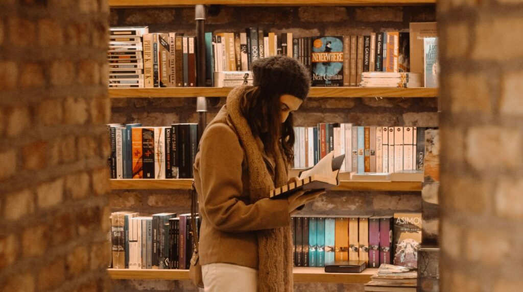 A woman looks at a book in a bookshop. The photo is framed by a brick arch.