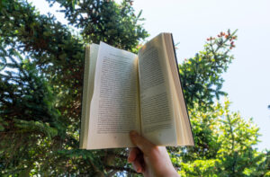 A person holding up a book with a tree in the background.