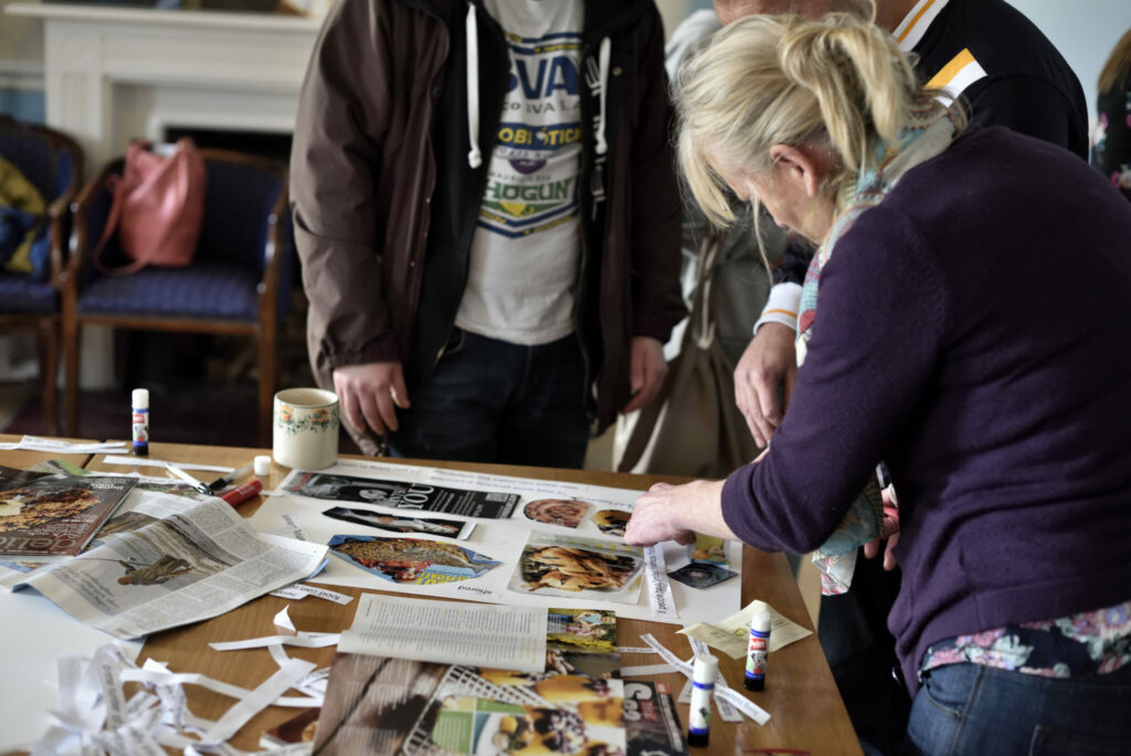 People round a table cutting and gluing images from magazines onto a piece of paper.