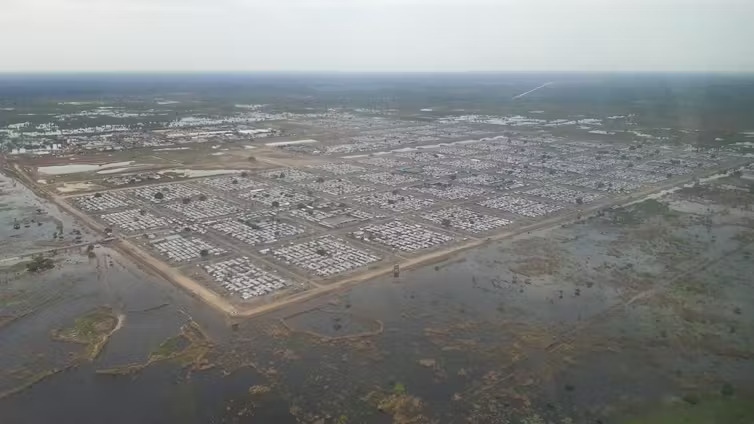 An aerial shot of an expansive refugee camp surrounded by flood water, barely contained by barriers.