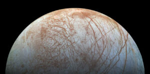 A shot of the moon Europa, an off-white hemisphere straked with rusty red patches.