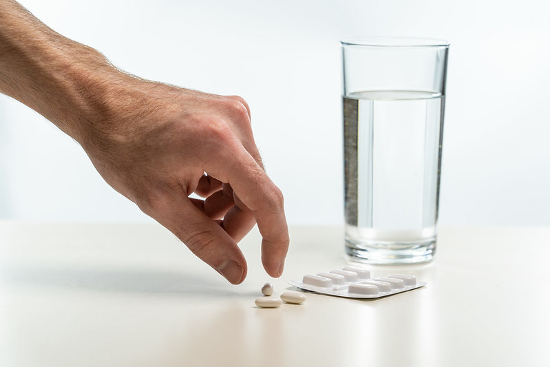 A person picking up a tablet with a glass of water in the background.