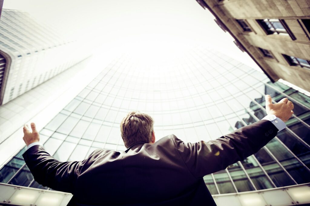 A businessman looking up at a corporate building with his arms spread out