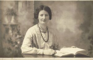 An antique photograph of a blackhaired woman holding an open book