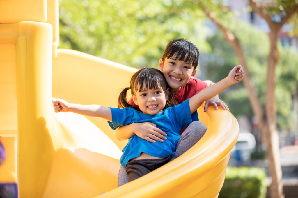 Asian Siblings playing at the playground, smiling and laughing