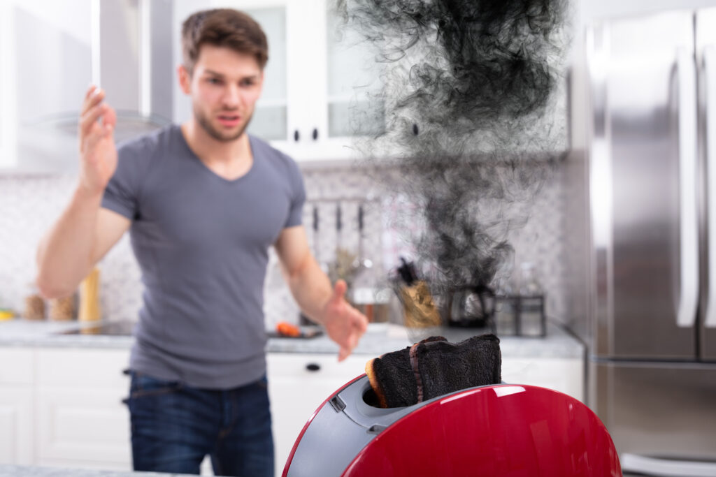 Frustrated Young Man Looking At Burnt Toasts In Toaster At Kitchen