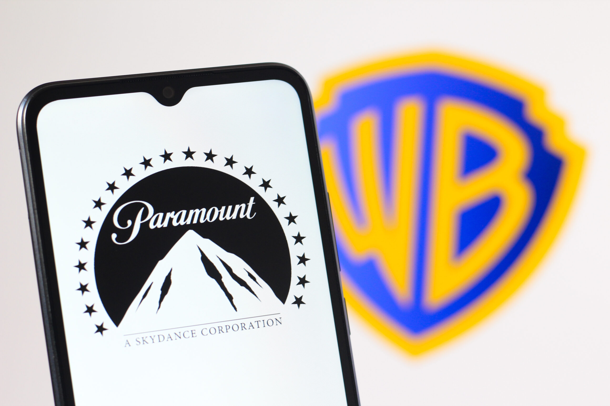In this photo illustration, the Paramount logo is seen displayed on a smartphone screen and the Warner Bros Discovery logo in the background