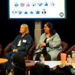 A panel of four diverse women sitting in front of a presentation screen